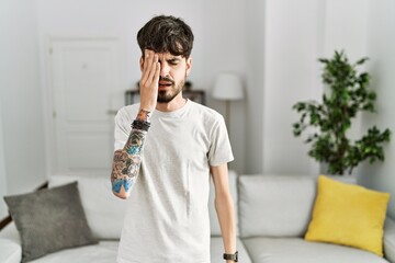 Poster - Hispanic man with beard at the living room at home yawning tired covering half face, eye and mouth with hand. face hurts in pain.