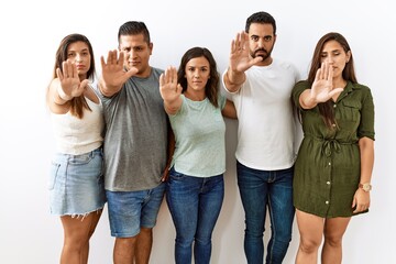 Wall Mural - Group of young hispanic friends standing together over isolated background doing stop sing with palm of the hand. warning expression with negative and serious gesture on the face.