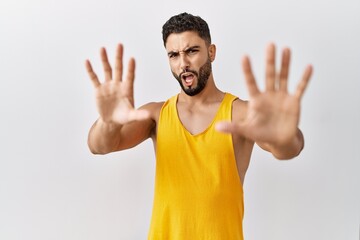 Wall Mural - Young handsome man with beard standing over isolated background afraid and terrified with fear expression stop gesture with hands, shouting in shock. panic concept.