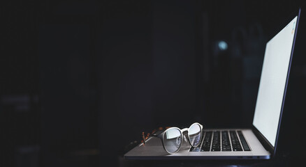 Wall Mural - Glasses near the laptop, reflect light from the screen in the dark, copy space.