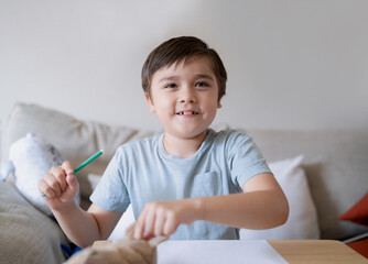Schoolboy using green colour pen drawing on white paper sheet, Young kid doing school homework, Happy mixed race child enjoy doing arts and playing with toys, Home Education
