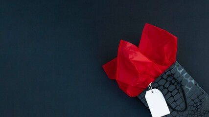 Wall Mural - Black gift bag with red tissue paper and white label on black background