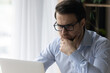 © fizkes - Close up serious thoughtful man in glasses looking at laptop screen, touching chin, pondering project strategy or analyzing statistics, focused businessman watching webinar, reading news in message