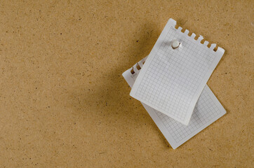 Sheets of paper hang vertically against the brown background. Torn blank sheets from the notepad on a spring. Side view. Copy space