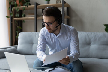 Canvas Print - Confident businessman in wireless headset and glasses talking, working, consulting client online about deal terms, holding documents, serious man engaged in internet meeting, conference at home