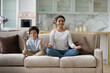 © fizkes - Happy small child boy sitting in lotus position on comfortable couch with joyful asian indian mother, practicing together yoga breathing exercise, doing asanas, enjoying domestic healthcare activity.