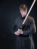 Fototapeta Tęcza - A villain with a red lightsaber, a young man in a long robe does fighting poses,
