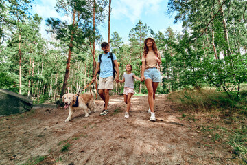 Wall Mural - Happy family with backpacks and labrador dog are walking in the forest. Camping, travel, hiking.