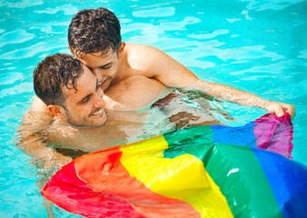 Gay couple relaxing in swimming pool with LGBT flag. Two young men enjoying nature outdoors, kissing and hugging. Young men romantic family in love. Happiness concept. 