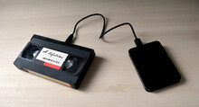 A Video Tape Labeled  As 'A Lifetime Memories' Plugged To A Hard Disk Drive As A Symbol Of Data Transfer From Analog To Digital.