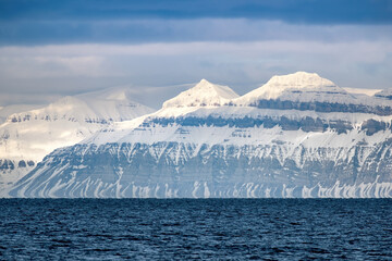 Wall Mural - the blue water of the nordfjorden fjord and the sunlit mountains of svalbard at dusk.