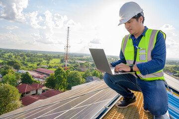 Wall Mural - Asian technician working on a solar power plant using a laptop computer to check the maintenance of solar panels on the roof.