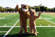 Two cougar mascots posing on the football field waving to the camera