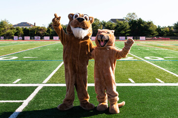 two cougar mascots posing on the football field waving to the camera