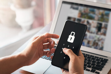 Hacking a Phishing mobile phone with a password to access a smartphone, security threats online, and fraud. A young man with a cell phone and laptop is secure in his bank account.