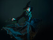 © Ulia Koltyrina - Witch in a long black dress dancing and conjuring, Halloween party.