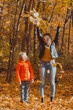 © satura_ - Single parent family playing with autumn leaves in park. Happy mom and son throw autumn leaves up in fall park.
