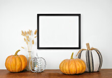 Mock Up Black Frame Hanging From A White Wall With Pumpkins And Fall Decor On A Wood Shelf. Autumn Concept. Copy Space.