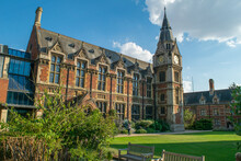View Of Historical Bricked Christ's College Building Attached To A Medieval Style Clock Tower In Front Of Lawn And Benches In Cambridge England