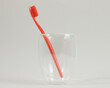 bright orange toothbrush in a transparent glass glass on a light neutral background, close-up
