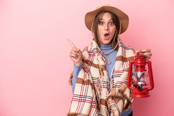 Wall Mural - Young caucasian woman holding vintage lantern isolated on pink background pointing to the side