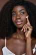 © insta_photos - Gorgeous African American 20s girl with afro hair applying putting moisturizing cream on face for perfect skin complexion doing daily routine. Skincare and cosmetology concept. Close up vertical.