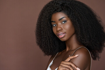 Stunning happy African American young woman with afro hair and perfect smooth skin complexion looks at camera touching shoulder with hand. Skincare, cosmetology and spa concept. Close up. Copy space.