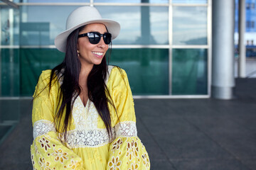 Poster - Pretty Hispanic woman in a yellow dress and dark sunglasses smiling in the street