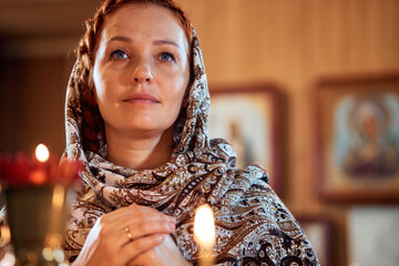 Wall Mural - a young woman in a headscarf prays in an Orthodox church and puts candles in front of icons