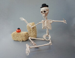 Skelton with Black Felt Hat Two Hay Bales and Pumpkin with Eyes on Gray Background