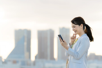 Poster - 都市を背景にスマホを見る女性