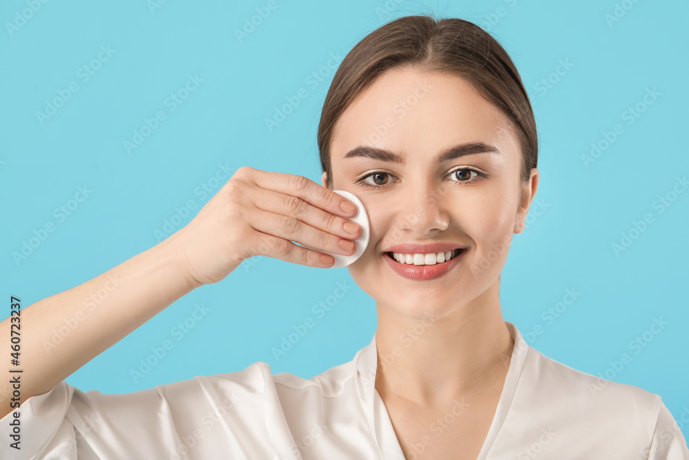 Beautiful young woman with cotton pad on color background
