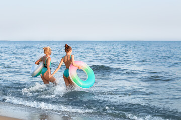 Canvas Print - Beautiful young women with inflatable rings on sea beach