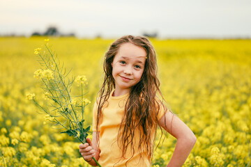 Wall Mural - Pretty long haired girl playing in vibrant canola field in full bloom