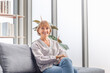 © JU.STOCKER - Portrait of Smiling mature woman sitting on a sofa at home, Happy relaxing elderly woman on the cozy sofa in living room
