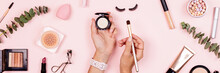 Flat Lay Of Professional Cosmetics Set On Pastel Pink Background. Woman Holding Hands Makeup Brush