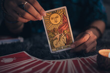 Fortune Teller Holding THE SUN Card And Tarot Cards. Tarot Cards And Burning Candles. Astrologists And Forecasting Concept.