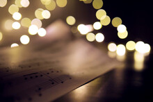 Old Sheet With Christmas Music Notes As Background Against Blurred Lights. Christmas Music Concept