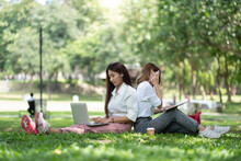 Happy Asian University Sitting Outside On Campus. Two Girl Working And Studying Together With Laptop And Digital Tablet In The Park.