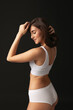© master1305 - Back view. Portrait of young beautiful slim woman in white lingerie, bra and panties isolated over dark background. Natural beauty concept.