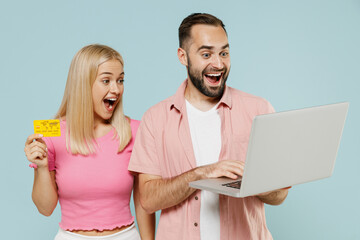 Young shocked couple two friends family man woman in casual clothes use laptop pc computer credit bank card shopping online booking tour together isolated on pastel plain light blue background studio.