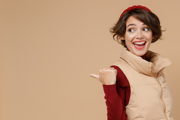 Wall Mural - Young smiling woman 20s wear red turtleneck vest beret point thumb finger aside on workspace area copy space mock up isolated on plain pastel beige background studio portrait People lifestyle concept