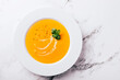 Flat lay of pumpkin soup on white background with cream and mint garnish