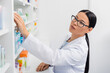 asian pharmacist in glasses reaching medication in drugstore