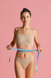 © master1305 - Portrait of young beautiful slim girl in lingerie takes measurements from yourself isolated over pink studio background.