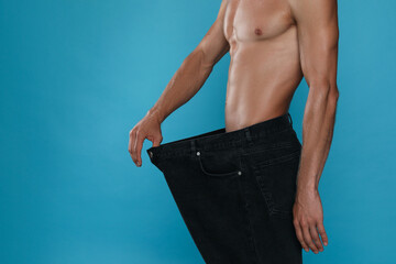 Wall Mural - Shirtless man with slim body wearing big jeans on light blue background, closeup