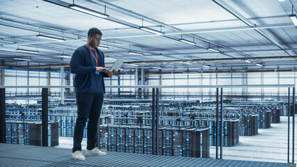 Leinwandbilder - Data Center Engineer Using Laptop Computer. Server Farm Cloud Computing Specialist Facility with African American Male System Administrator Working with Data Protection Network for Cyber Security.