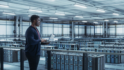 Wall Mural - Data Center Engineer Using Laptop Computer. Server Farm Cloud Computing Specialist Facility with African American Male System Administrator Working with Data Protection Network for Cyber Security.