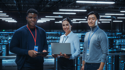 Leinwandbilder - Diverse Team of Data Center System Administrators and IT Specialists Use Laptop and Tablet Computers, Smiling on Camera. IT Engineers work on Cyber Security Protection in Cloud Computing Server Farm.