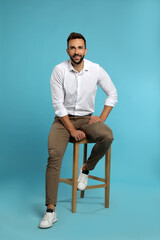 Wall Mural - Handsome man sitting on stool against turquoise background